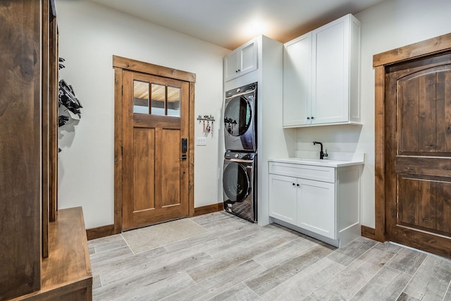laundry area featuring stacked washer / dryer, cabinet space, light wood-style flooring, and baseboards