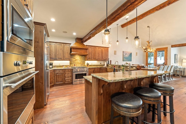 kitchen featuring appliances with stainless steel finishes, custom range hood, a breakfast bar area, beam ceiling, and light wood finished floors