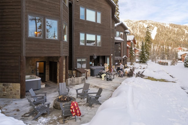 snow covered house featuring a fire pit, cooling unit, a patio, a mountain view, and stone siding