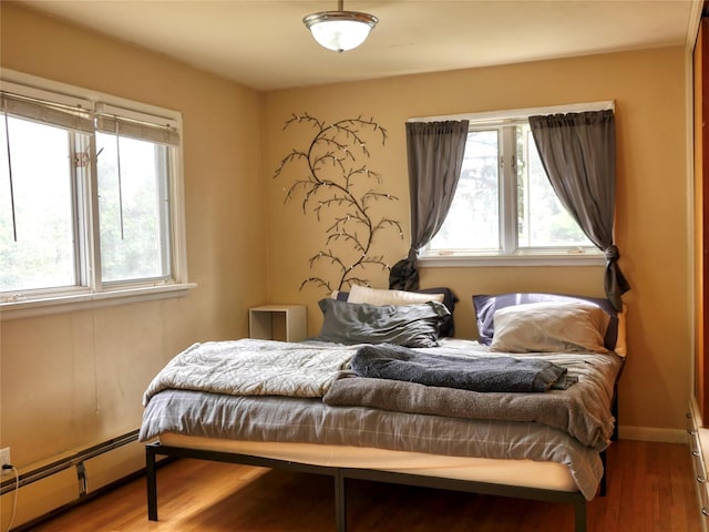 bedroom featuring a baseboard radiator, multiple windows, and wood finished floors