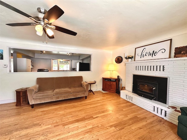 living area with wood finished floors, baseboards, a brick fireplace, and a ceiling fan