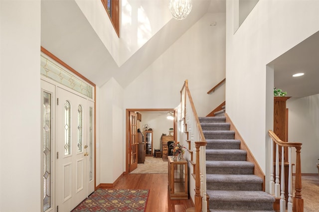 foyer entrance featuring a high ceiling, stairs, wood finished floors, baseboards, and a chandelier