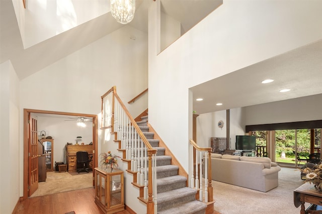 stairway with a towering ceiling, recessed lighting, a chandelier, wood finished floors, and carpet flooring