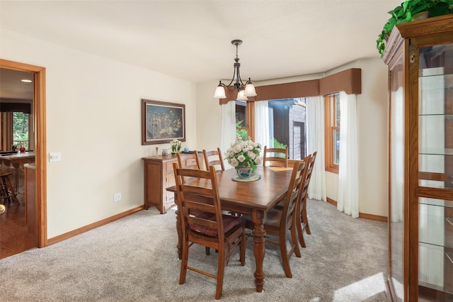 dining space featuring light colored carpet, baseboards, and a chandelier