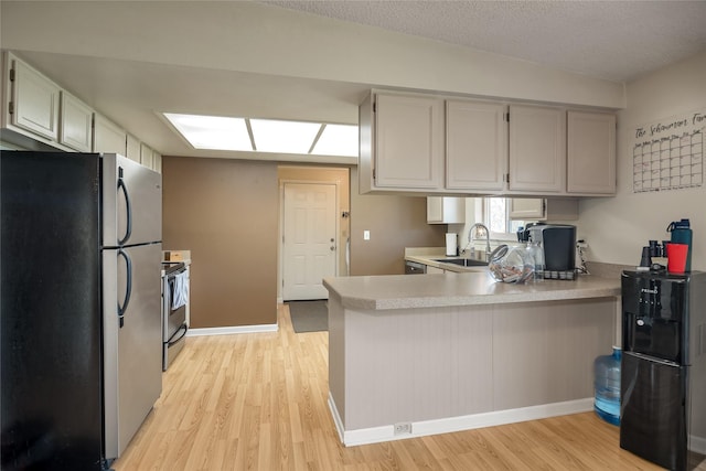 kitchen featuring appliances with stainless steel finishes, a sink, a peninsula, light wood finished floors, and light countertops