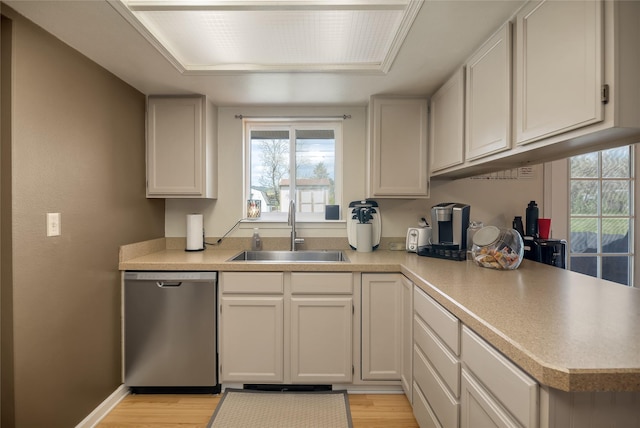 kitchen featuring stainless steel dishwasher, a sink, light wood-type flooring, and plenty of natural light