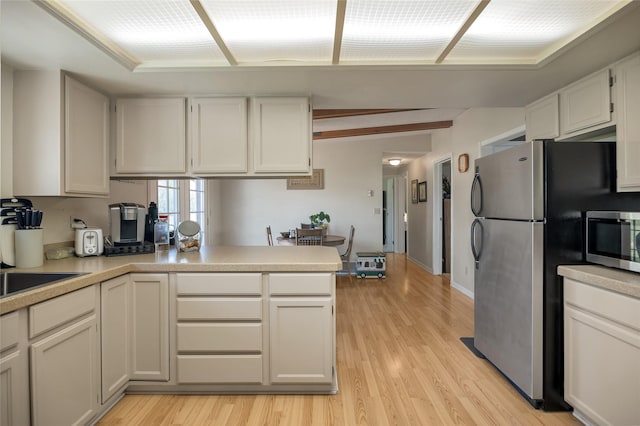 kitchen with appliances with stainless steel finishes, light wood-style flooring, light countertops, and a peninsula