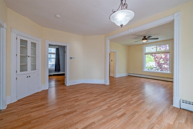 spare room with a baseboard radiator, healthy amount of natural light, light wood finished floors, and a ceiling fan