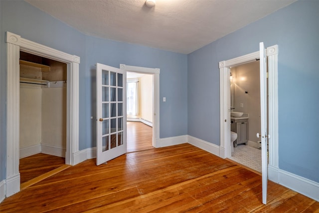 unfurnished bedroom featuring hardwood / wood-style flooring, baseboards, french doors, a closet, and ensuite bath