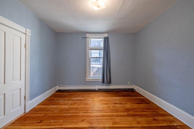 empty room featuring wood-type flooring, a baseboard heating unit, and baseboards