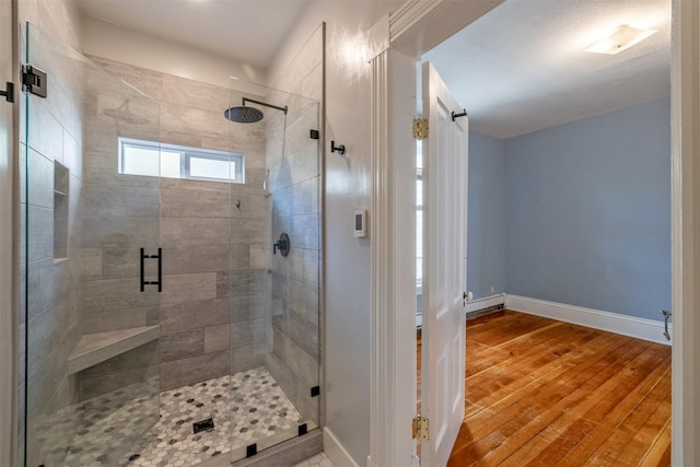 bathroom with a baseboard heating unit, baseboards, a stall shower, and wood finished floors