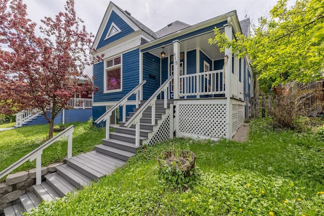 view of front of property featuring stairway, covered porch, and a front lawn