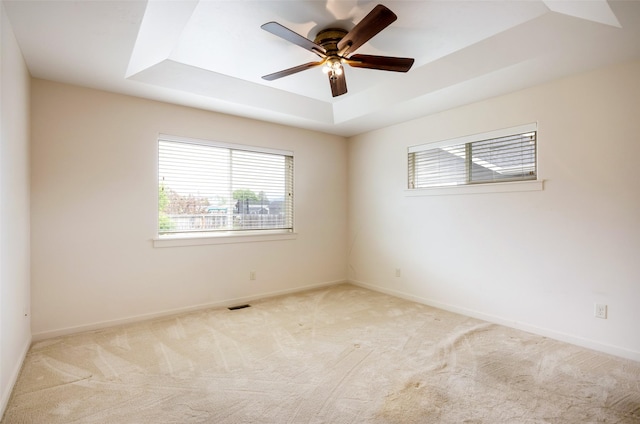 empty room featuring a tray ceiling, ceiling fan, carpet flooring, and baseboards