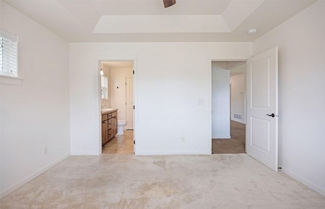 unfurnished bedroom featuring light colored carpet, baseboards, and a raised ceiling