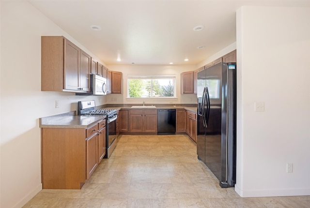 kitchen with appliances with stainless steel finishes, baseboards, a sink, brown cabinetry, and recessed lighting