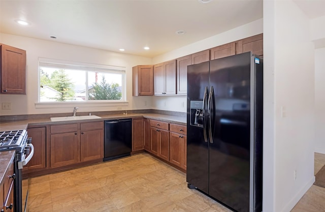 kitchen featuring black appliances, a sink, brown cabinets, dark countertops, and recessed lighting
