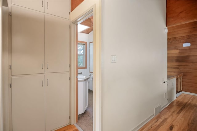 hallway featuring light wood-style flooring, an upstairs landing, and wooden walls
