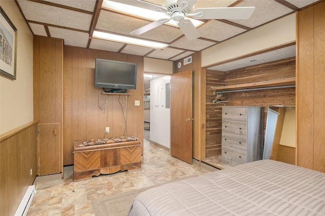 bedroom featuring wooden walls, a baseboard radiator, a closet, stone finish floors, and electric panel