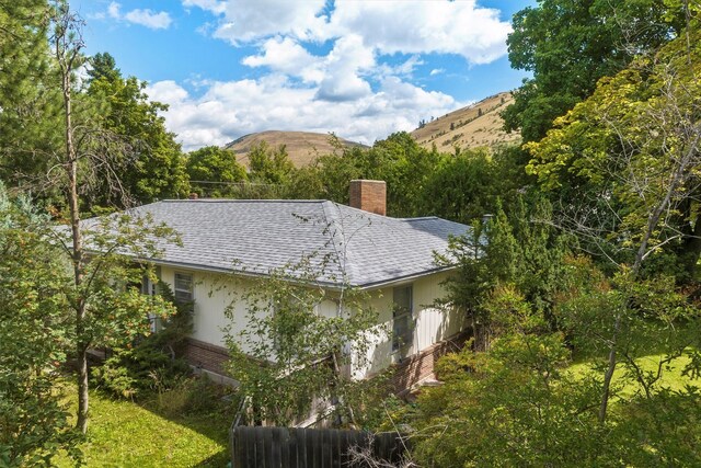 view of side of property featuring brick siding, a chimney, roof with shingles, a mountain view, and fence