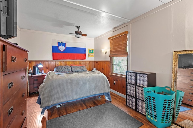 bedroom featuring wood finished floors, a wainscoted wall, ceiling fan, and wooden walls