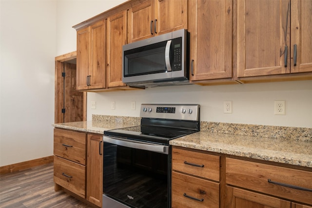 kitchen with stainless steel appliances, brown cabinetry, dark wood-style flooring, baseboards, and light stone countertops