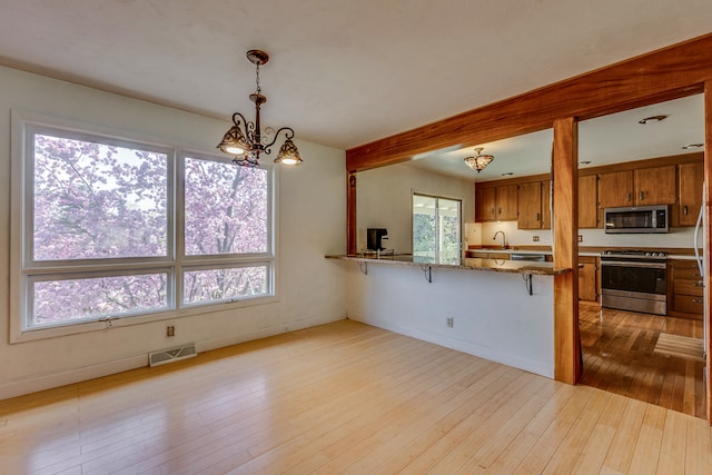 2046 Fairway Dr, Billings, MT 59102 - kitchen featuring appliances with stainless steel finishes, brown cabinetry, a sink, light wood-style floors, and a chandelier