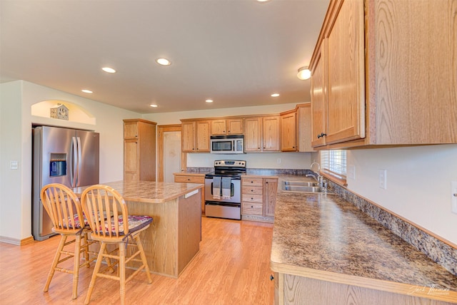 kitchen with appliances with stainless steel finishes, a sink, a breakfast bar area, light wood-type flooring, and recessed lighting