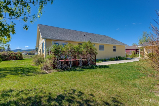 rear view of property featuring a lawn, a patio area, and roof with shingles