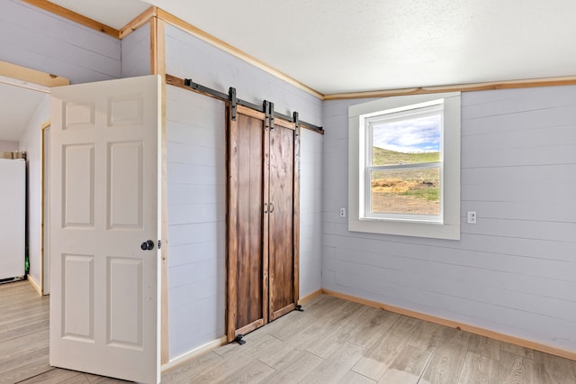 49 Embry Ln, Great Falls, MT 59404 - unfurnished bedroom featuring a barn door, light wood-type flooring, freestanding refrigerator, and wooden walls