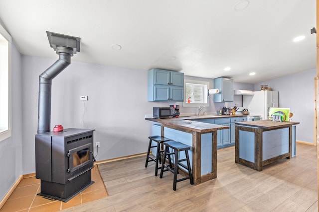 49 Embry Ln, Great Falls, MT 59404 - kitchen with butcher block counters, blue cabinets, a wood stove, white refrigerator with ice dispenser, and light wood-style floors
