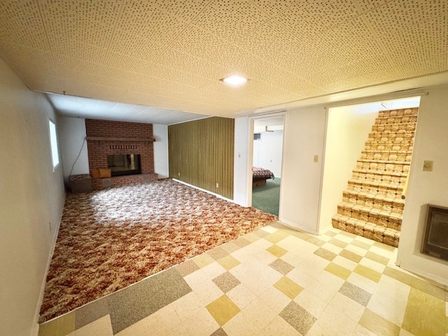 unfurnished living room featuring stairs, a brick fireplace, tile patterned floors, and plenty of natural light