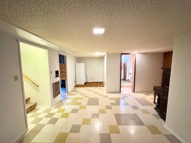 finished basement featuring light floors, stairs, baseboards, and freestanding refrigerator