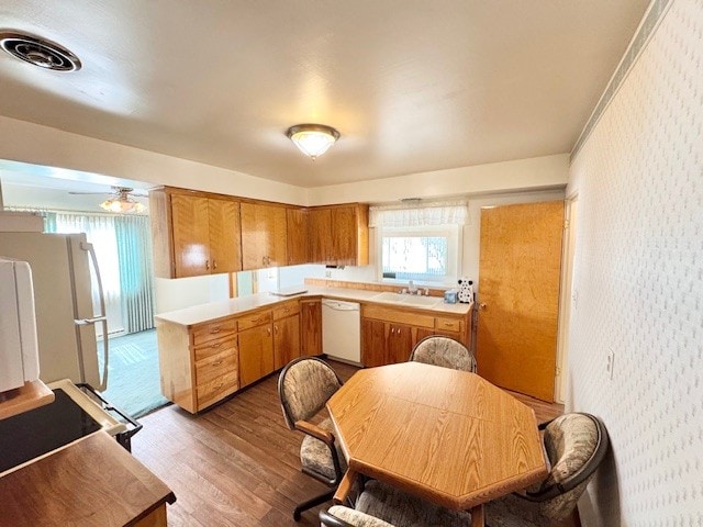 kitchen with white appliances, wood finished floors, light countertops, wallpapered walls, and brown cabinetry