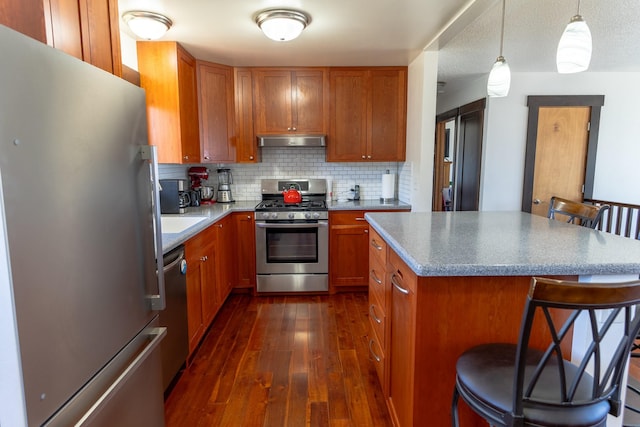 1827 Hollins Ave, Helena, MT 59601 - kitchen with appliances with stainless steel finishes, under cabinet range hood, brown cabinetry, and dark wood-type flooring