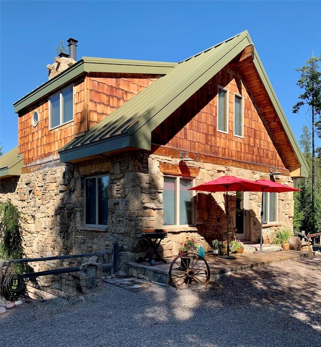 237 N Monture Ct, Seeley Lake, MT 59868 - view of front of house with stone siding, a standing seam roof, a chimney, and metal roof