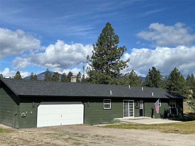 5061 Falcon Ln, Stevensville, MT 59870 - view of front of house featuring dirt driveway, a chimney, an attached garage, and a patio area