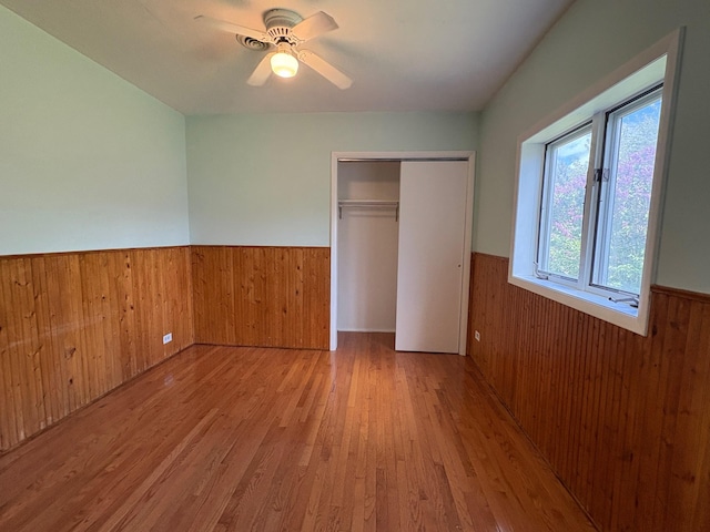 330 N Walnut St, Dillon, MT 59725 - unfurnished bedroom with wainscoting, wood walls, wood finished floors, a closet, and ceiling fan