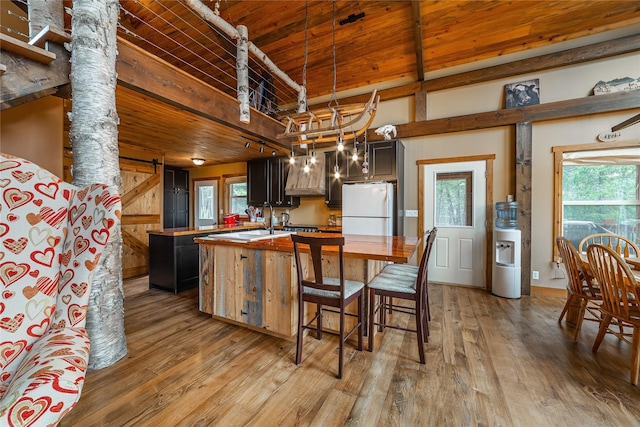 277 Ridge Loop Rd, Rexford, MT 59930 - kitchen featuring freestanding refrigerator, wooden ceiling with exposed beams, a kitchen island with sink, light wood-style floors, and custom range hood