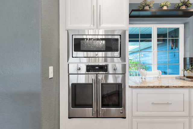 5634 Fairview Ln, Florence, MT 59833 - kitchen featuring appliances with stainless steel finishes, a textured wall, white cabinets, and light stone countertops