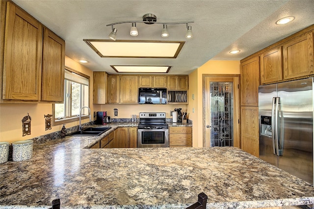 31521 Mcdonald Lake Rd, Saint Ignatius, MT 59865 - kitchen featuring appliances with stainless steel finishes, a sink, brown cabinetry, a peninsula, and a textured ceiling
