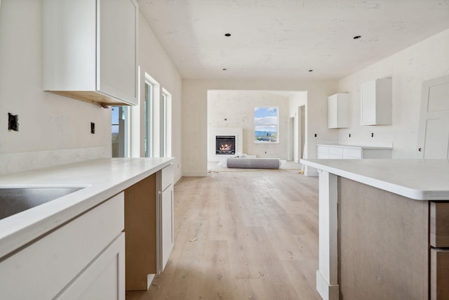 623 Holstein Way, Kalispell, MT 59901 - kitchen featuring light wood-style floors, white cabinetry, a lit fireplace, and light countertops