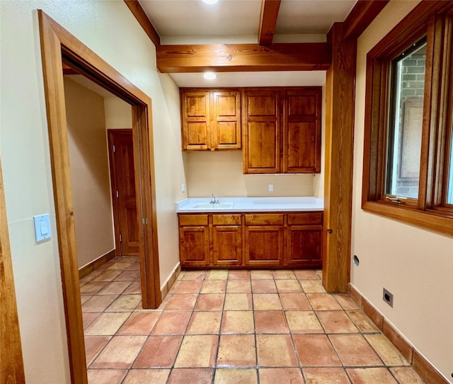 444 Windwalker Trl, Stevensville, MT 59870 - kitchen featuring brown cabinetry, light countertops, beam ceiling, a sink, and baseboards