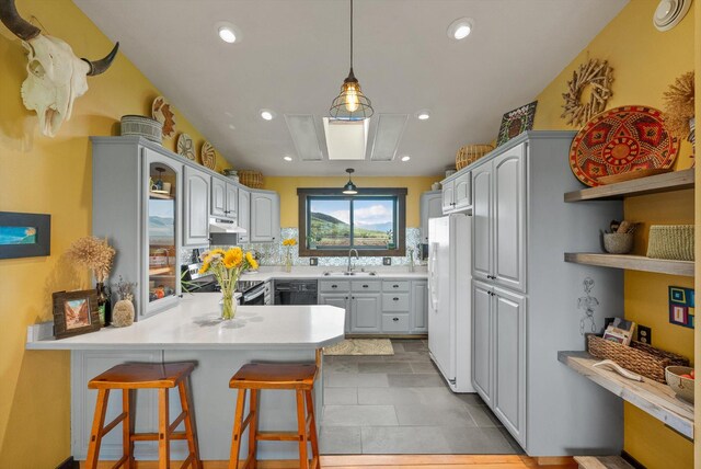 51943 Kuntz Ln, Charlo, MT 59824 - kitchen with freestanding refrigerator, a peninsula, under cabinet range hood, a sink, and decorative backsplash