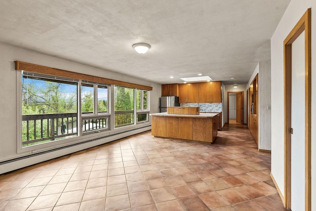 160 Sherwood Ln, Kalispell, MT 59901 - kitchen with freestanding refrigerator, decorative backsplash, light countertops, brown cabinetry, and a baseboard heating unit