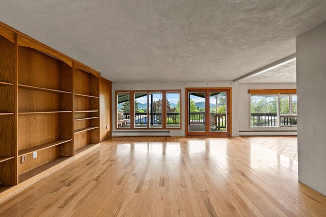 160 Sherwood Ln, Kalispell, MT 59901 - unfurnished living room featuring baseboard heating, a baseboard radiator, light wood-style flooring, built in shelves, and a textured ceiling