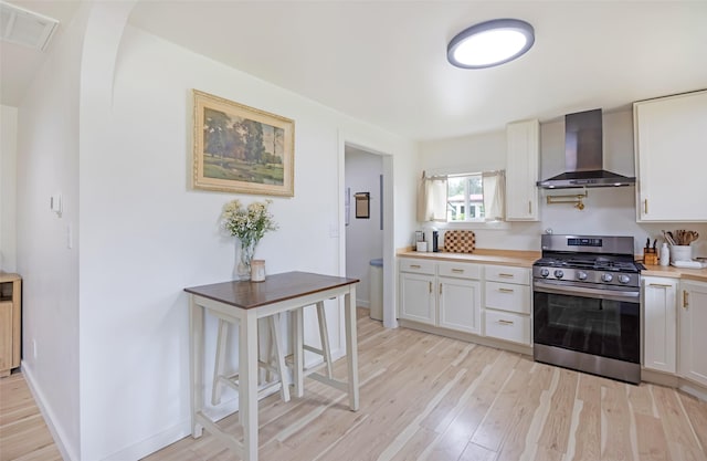 215 Tower St, Missoula, MT 59804 - kitchen featuring stainless steel gas range, wall chimney exhaust hood, light wood-type flooring, white cabinetry, and baseboards