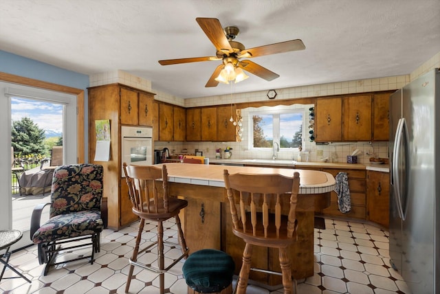 30 Panoramic Dr, Kalispell, MT 59901 - kitchen featuring stainless steel fridge with ice dispenser, light floors, white oven, tile counters, and brown cabinets