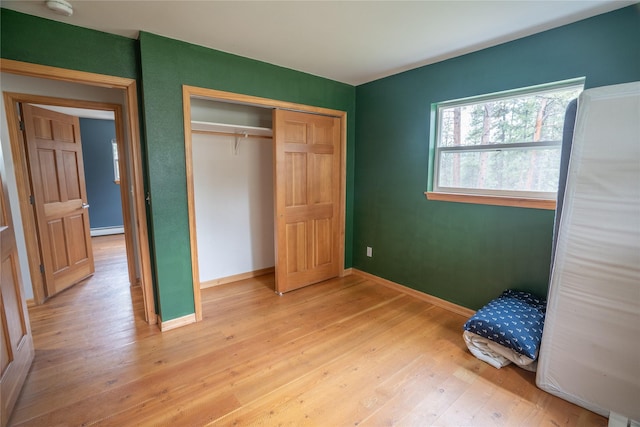 3185 Hubbart Dam Rd, Marion, MT 59925 - unfurnished bedroom featuring light wood-style floors, a baseboard heating unit, a closet, and baseboards