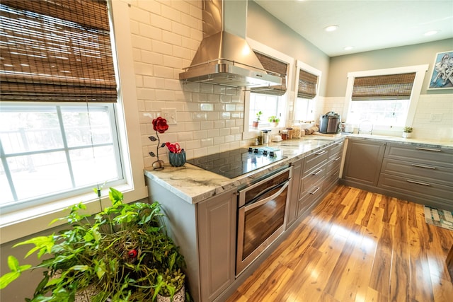1610 Maple Dr, Fort Benton, MT 59442 - kitchen with stainless steel oven, wall chimney exhaust hood, black electric cooktop, healthy amount of natural light, and recessed lighting