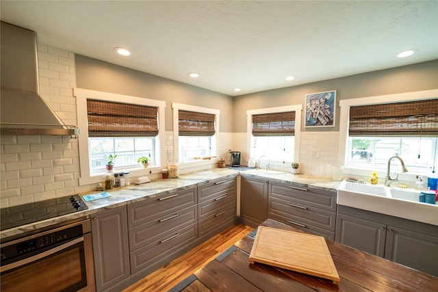 1610 Maple Dr, Fort Benton, MT 59442 - kitchen featuring stainless steel oven, wall chimney exhaust hood, gray cabinets, wood finished floors, and black electric stovetop